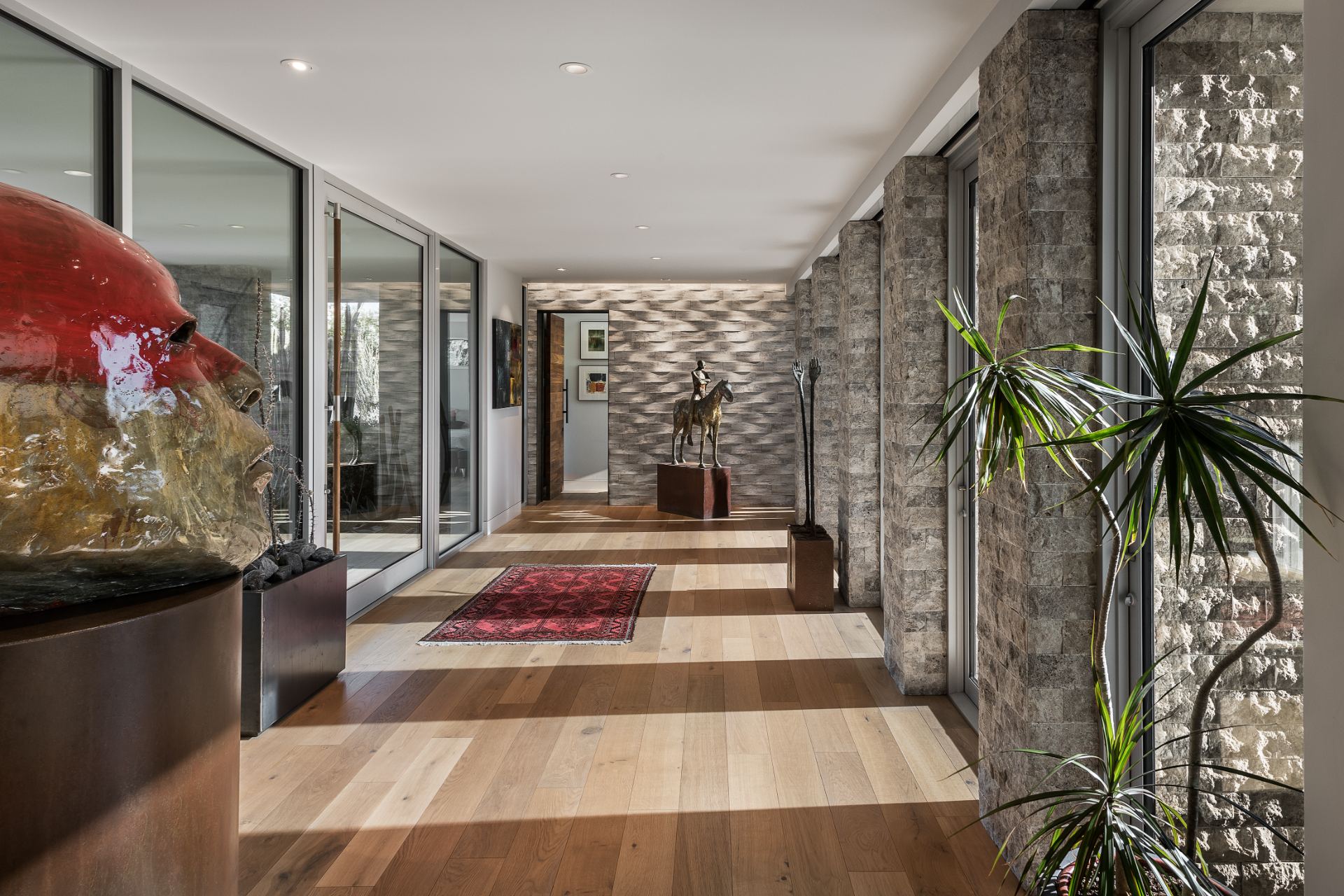 Gallery-style entry hall of a project home with split-stone columns, wide-plank oak floors and collected sculpture