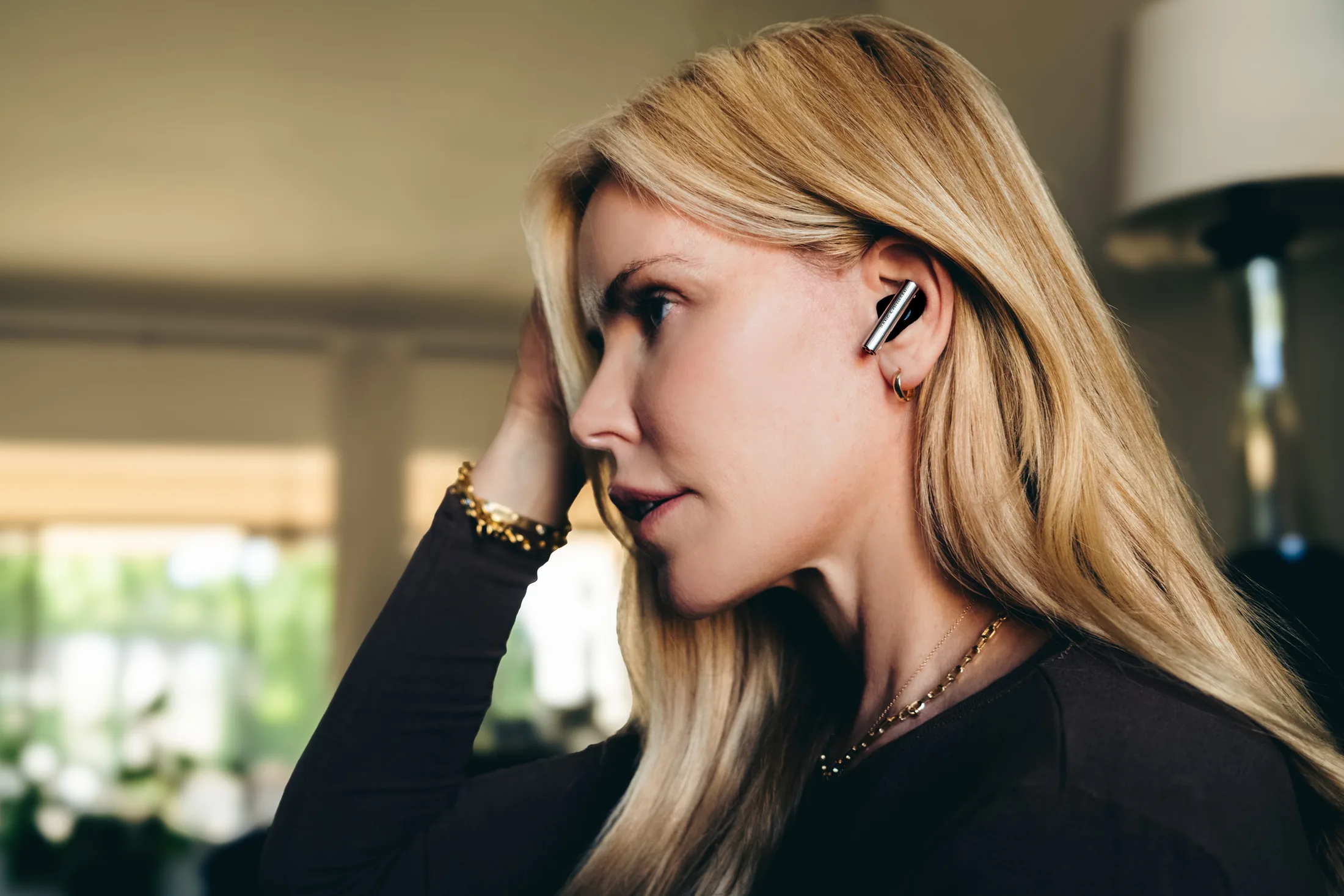 Woman in profile wearing Bang & Olufsen earbuds in a softly lit living room