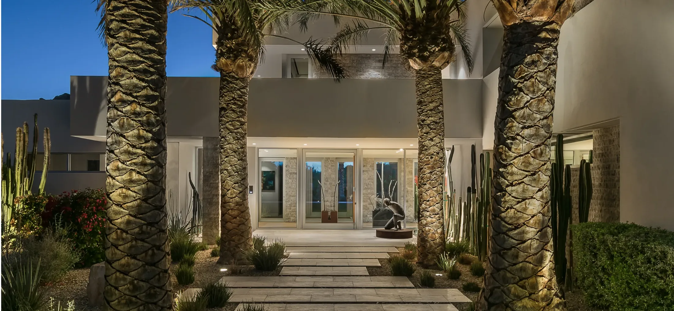 Entry courtyard of a desert home at dusk, palm trunks and path lighting leading to the front door