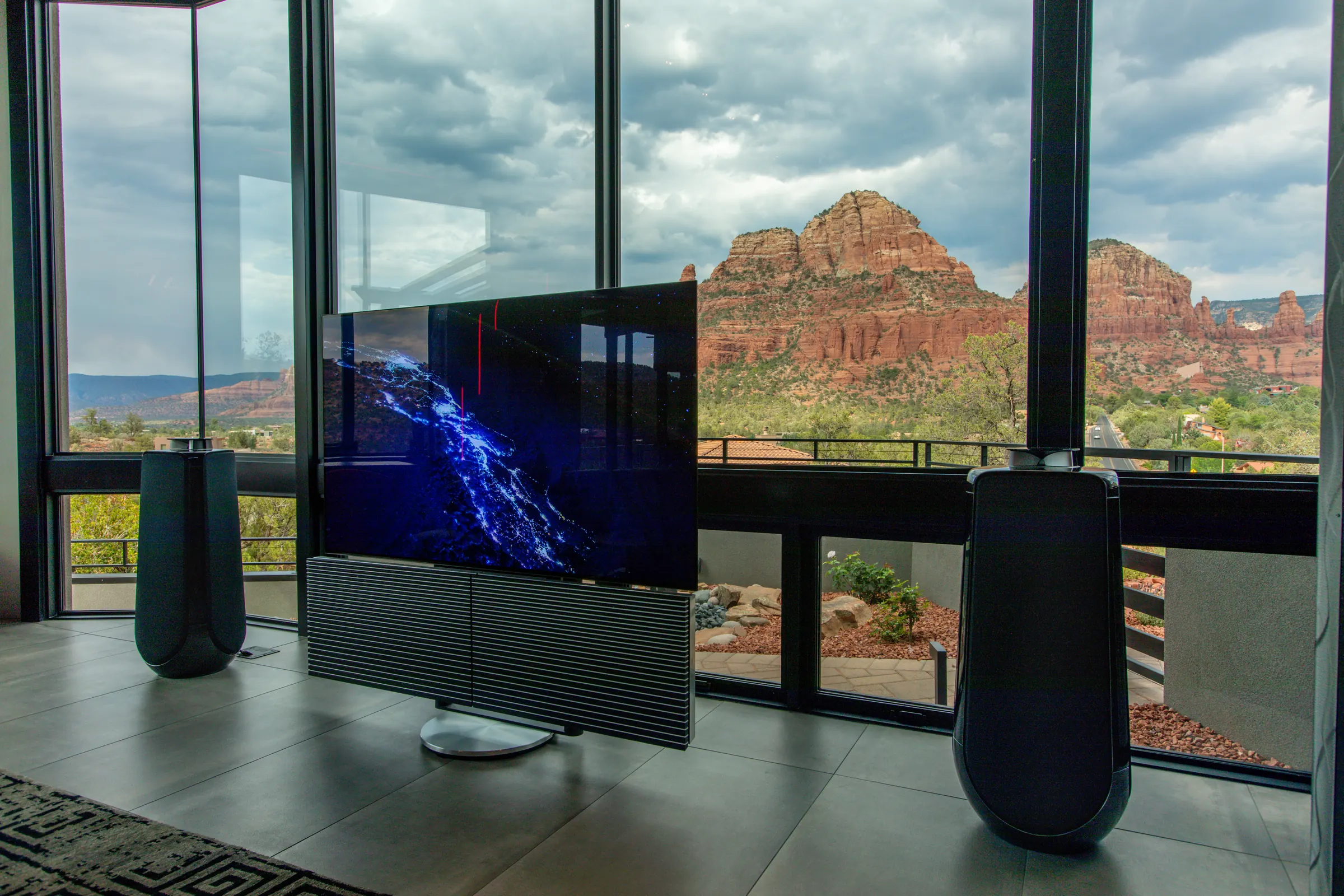 Beovision Harmony unfolding between two Beolab 50 speakers, Sedona red rocks beyond the glass