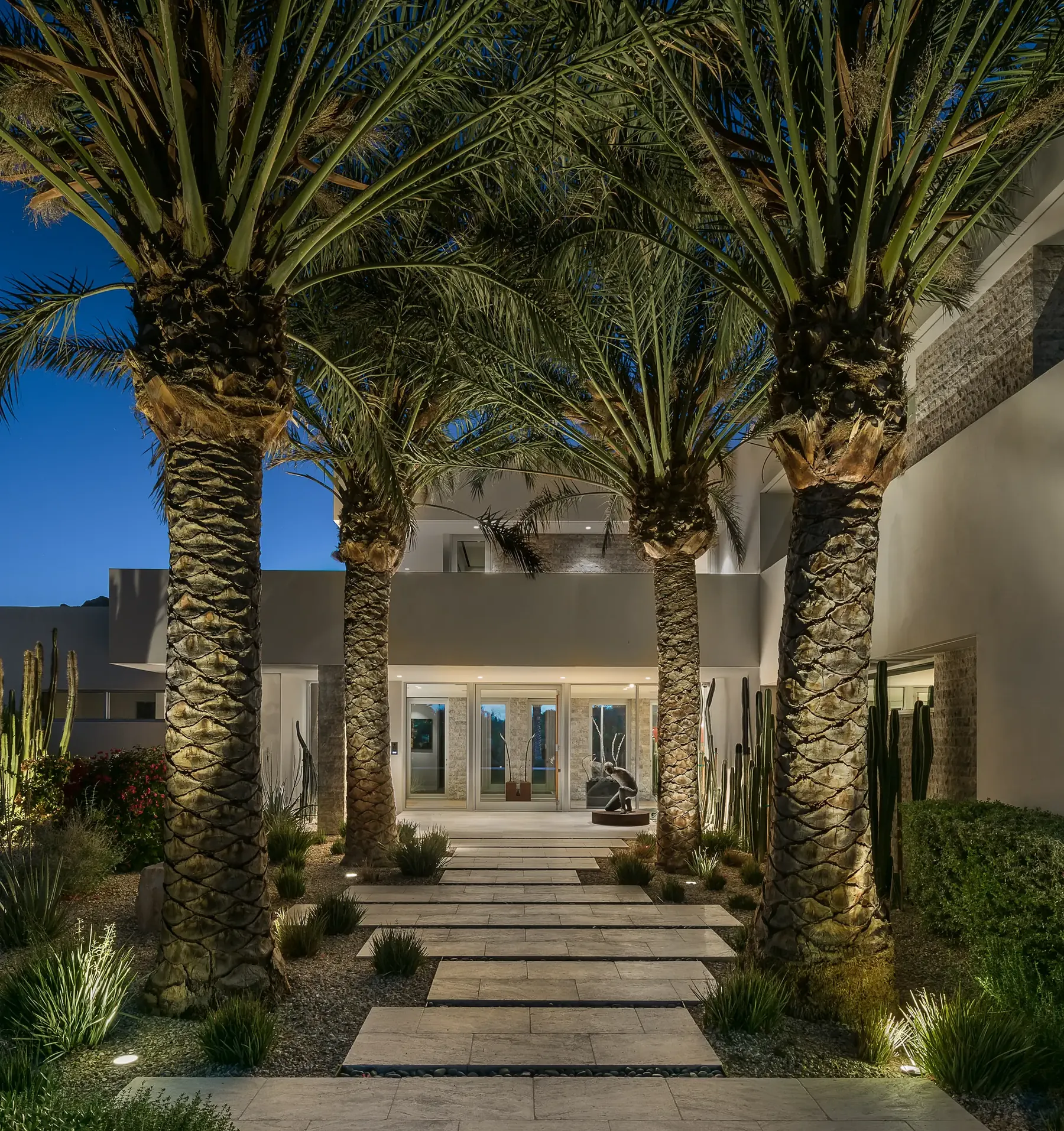 Landscape lighting at dusk — uplit palms and path lights along the front walkway of a Watt Integration project home, Paradise Valley